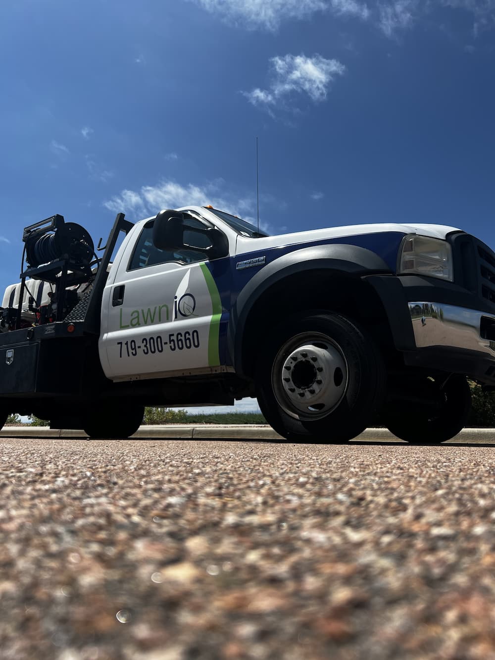 A LawnIQ service truck is parked on a street under a blue sky. The truck displays the company logo and phone number, 719-300-5660, on the driver’s side door. The vehicle appears ready for landscaping work.